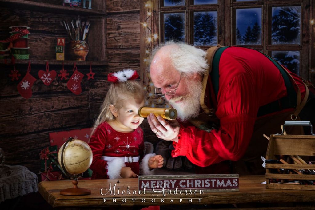A little girl gets to peek in Santa's magic kaleidoscope at The Best Santa Experience in Mounds View, MN.