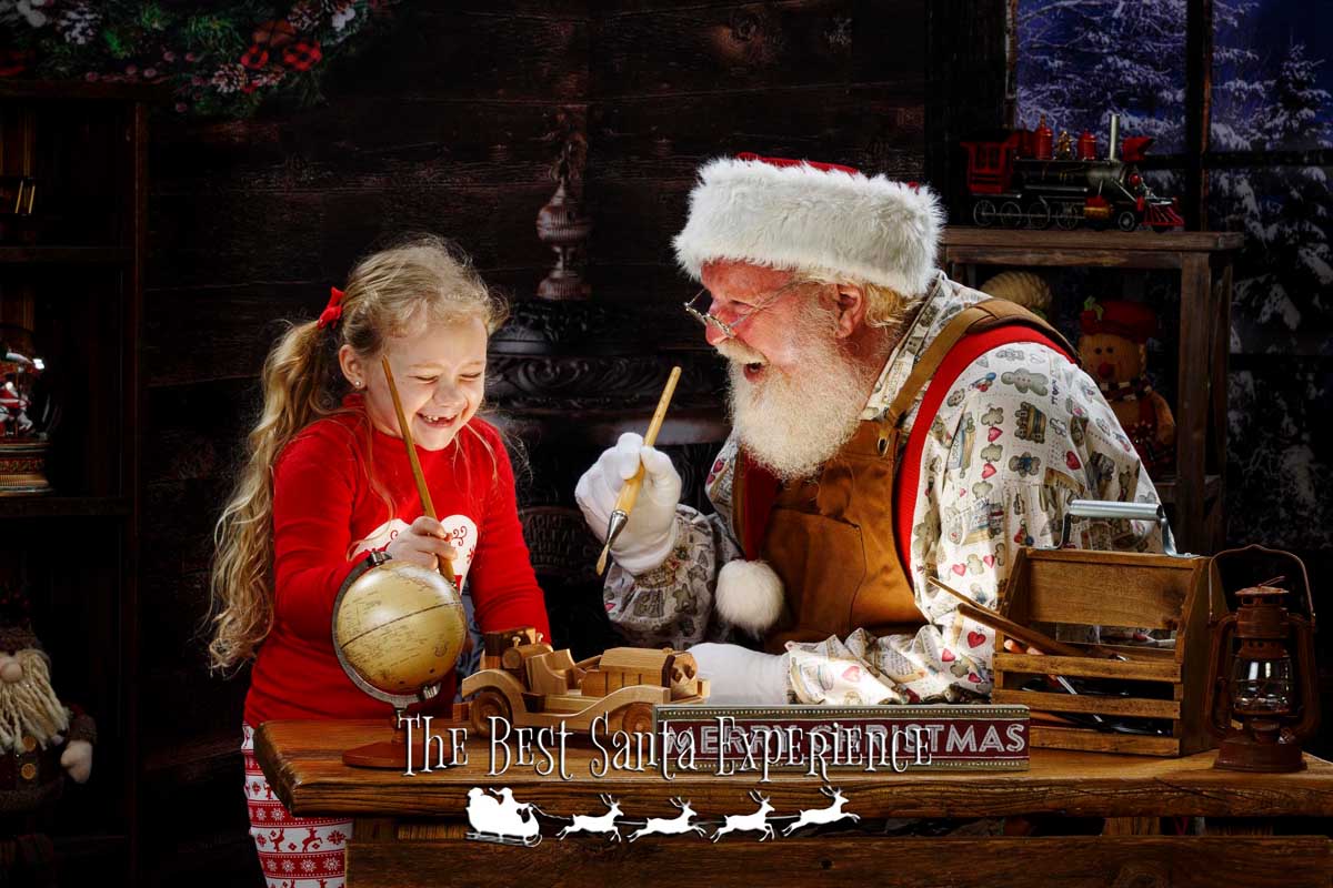 An adorable girl and Santa share a big laugh while painting toys in his workshop at The Best Santa Experience.
